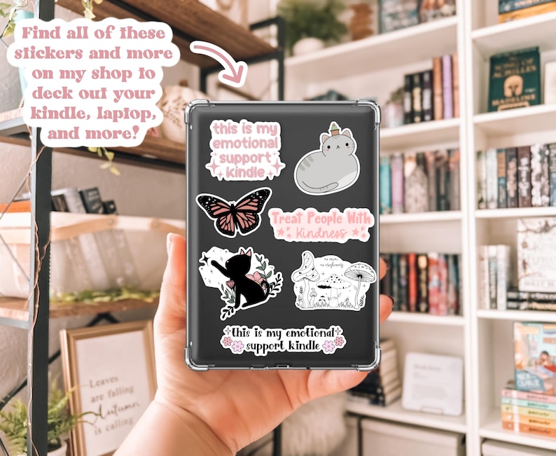 Może przedstawiać: Przezroczyste etui z naklejkami na Kindle. Naklejki obejmują motyla, kota, grzyba i tekst z napisem "this is my emotional support kindle" i "Treat People With Kindness". Obraz zawiera r&oacute;wnież tekst z napisem "Find all of these stickers and more on my shop to deck out your kindle, laptop, and more?"