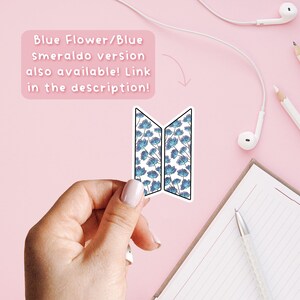 Może przedstawiać: Naklejka z niebiesko-białym kwiatowym wzorem, trzymana na r&oacute;żowym tle. Obraz zawiera tekst: "Blue Flower/Blue Smeraldo version also available! Link in the description!" Widoczny jest r&oacute;wnież notatnik i słuchawki.