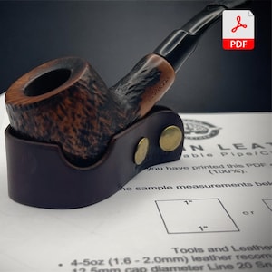 Könnte beinhalten: Eine Tabakpfeife aus Holz mit dunkelbraunem Finish liegt in einem dunkelbraunen Lederhalter. Die Pfeife hat ein schwarzes Mundstück und einen strukturierten Kopf. Der Lederhalter ist mit zwei messingfarbenen Nieten befestigt. Das Bild enthält ein PDF-Symbol.