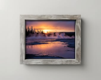 May include: Framed landscape photograph of a sunrise over a geothermal area. The image features a vibrant orange and purple sky, with steam rising from the water. The frame is made of weathered gray wood.