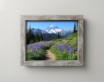 May include: A framed landscape print featuring a mountain scene. A dirt path winds through a field of purple wildflowers towards a snow-capped mountain under a clear blue sky. The frame is made of weathered wood.