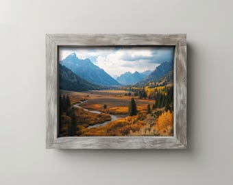 May include: A framed landscape photograph featuring a valley with a river, mountains, and trees. The photograph is in a rustic gray wooden frame. The scene includes blue mountains, a winding river, and golden-yellow trees.