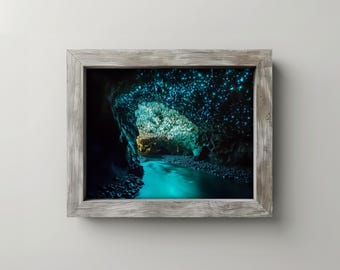 May include: A framed print of a cave with a river. The cave's ceiling is illuminated with blue lights, and the water glows turquoise. The frame is made of weathered gray wood, adding a rustic touch to the artwork.