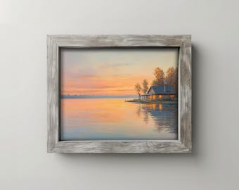 Pode incluir: Pintura emoldurada de uma paisagem lacustre ao pôr do sol. O céu transita do laranja para o amarelo, refletindo-se na água. Uma cabana com janelas iluminadas está na margem, ladeada por árvores. A moldura é cinza desgastado.