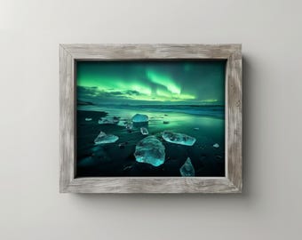 Pode incluir: Uma impressão emoldurada mostrando uma paisagem vibrante. A imagem captura a aurora boreal com tons verdes e brancos sobre uma praia com formações de gelo espalhadas. A moldura é de madeira desgastada.