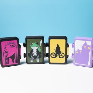 Peut inclure: Quatre briquets rectangulaires noirs avec des motifs graphiques uniques. Les motifs comprennent une illustration rose d'une femme, une grenouille fumant, un cycliste et une illustration de chat violet.