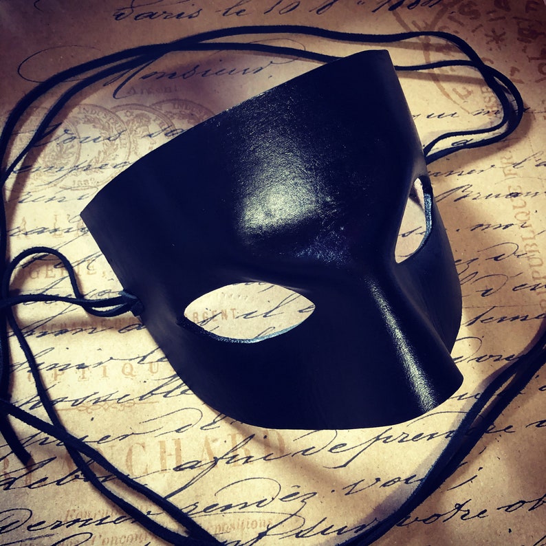 May include: A black leather masquerade mask with a single eye hole and a long, flowing strap.