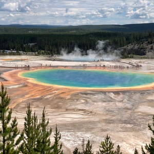 May include: An aerial view of the Grand Prismatic Spring in Yellowstone National Park. The spring features vibrant colors, including blue, orange, and yellow. Steam rises from the water, and a boardwalk allows visitors to walk around the spring.