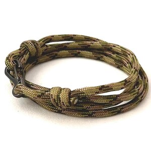 May include: Camouflage pattern paracord bracelet with a black metal clasp. The bracelet is made of multiple strands of rope, knotted together. The colors include shades of green, brown, and tan.