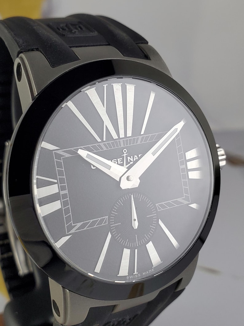May include: A dark grey wristwatch with a black bezel and a black rubber strap. The watch face is grey with white Roman numerals and hands. The words "SWISS MADE" are printed at the bottom of the watch face.