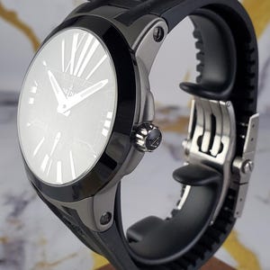 May include: A contemporary wristwatch featuring a black rubber strap and a silver-toned case. The watch face is light-coloured with Roman numeral hour markers and silver hands. The watch has a black bezel and a decorative crown.