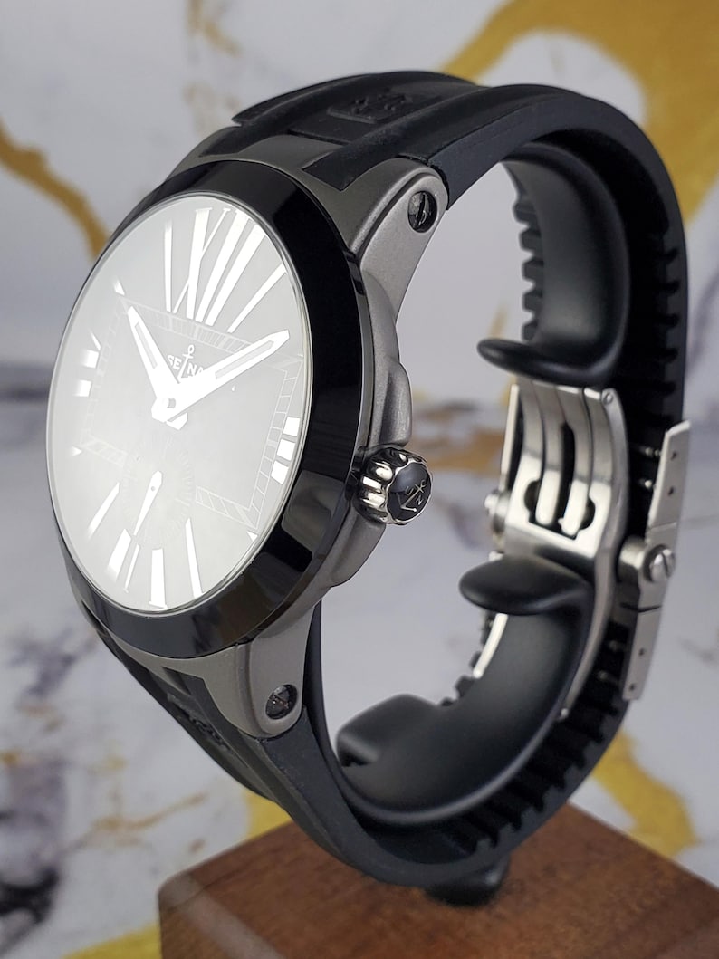 May include: A contemporary wristwatch featuring a black rubber strap and a silver-toned case. The watch face is light-coloured with Roman numeral hour markers and silver hands. The watch has a black bezel and a decorative crown.