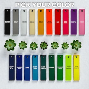 May include: A selection of colorful rectangular tags, each labeled with a different color name, including black, gray, white, and neon yellow. The text "PICK YOUR COLOR" is at the top. Small green succulents are interspersed between the tags.
