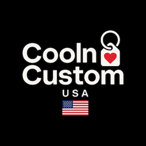 May include: The words "Cooln Custom" in white, with "USA" below, and an American flag graphic on a black background. A white tag with a red heart is attached to a keyring.