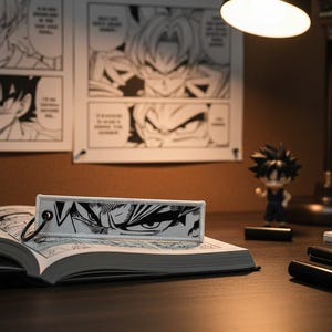 May include: A black and white manga-style bookmark featuring a close-up of a character's eyes, resting on an open book. The scene includes a figurine, a desk lamp, and manga panels on the wall, creating a themed workspace.