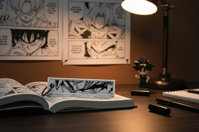 May include: A black and white manga-style bookmark featuring a close-up of a character's eyes, resting on an open book. The scene includes a figurine, a desk lamp, and manga panels on the wall, creating a themed workspace.