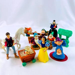 Könnte beinhalten: Eine Sammlung von Kunststofffiguren mit Schneewittchen, dem Prinzen, der bösen Königin und mehreren Zwergen. Das Set enthält ein weißes Pferd, einen braunen Minenwagen mit klaren Kristallen und eine grüne Struktur. Jede Figur ist bemalt.