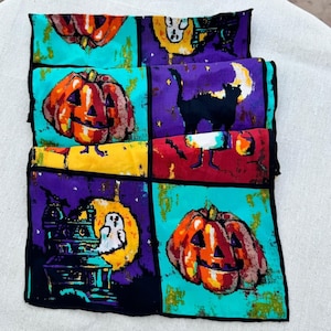 Peut inclure: Un tissu plié sur le thème d'Halloween avec un motif répété de citrouilles, de chats noirs, de fantômes et de maisons hantées. Le tissu présente une palette de couleurs orange, violet, sarcelle, jaune et noir. Le design rappelle l'esthétique vintage d'Halloween.