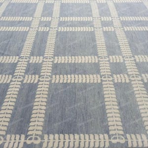 May include: A blue and white patterned rug. The rug features a grid design with white leaf-like patterns forming the grid lines. The background is a solid light blue color, creating a contrasting effect. The rug is likely made of woven material.