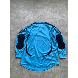 May include: A long-sleeved, light blue athletic jersey with black accents. The jersey has black padded sections on the elbows and a curved black design down the sides. The jersey is laid flat on a gray surface.