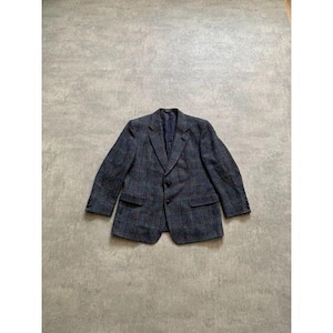 Op de afbeelding: Een marineblauwe blazer met een ruitpatroon. De blazer heeft twee voorzakken, een revers en een sluiting met twee knopen. De blazer is gemaakt van een textuurstof en ligt plat op een grijze ondergrond.