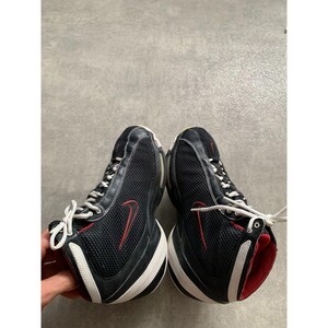 Puede incluir: Par de zapatillas deportivas negras y rojas con cordones y suelas blancas. Las zapatillas presentan una parte superior de malla con un logotipo de Nike rojo y detalles. Las suelas tienen un dise&ntilde;o curvo con rayas blancas y negras.