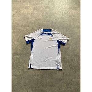 May include: White and blue athletic jersey with short sleeves. The jersey has blue detailing on the shoulders and sides, a small logo on the chest, and a Nike swoosh. The shirt is made of a lightweight, breathable material.