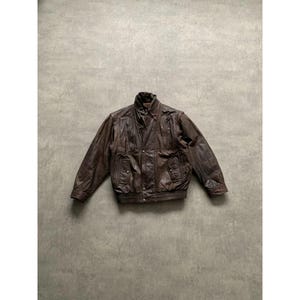 May include: A brown leather jacket with a ribbed hem and cuffs. The jacket has a collared neckline and two front pockets. The leather has a distressed appearance. The jacket is a vintage style.