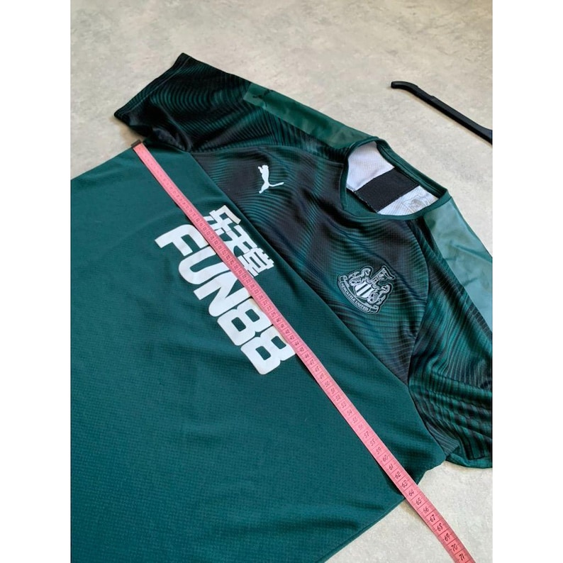 May include: A dark green and black soccer jersey with the text "FUN88" in white. The jersey has a Puma logo and a team crest. A pink measuring tape is laid across the jersey.