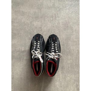 Puede incluir: Par de zapatillas deportivas negras con cordones blancos y detalles rojos. Las zapatillas tienen una parte superior de malla y un peque&ntilde;o logotipo rojo de Nike. Las suelas son blancas y el interior es rojo.