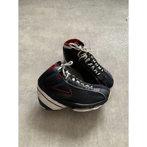 Puede incluir: Par de zapatillas deportivas altas negras y rojas con cordones y suelas blancas. Las zapatillas presentan un logotipo Nike swoosh rojo en el lateral y un forro interior rojo. Las suelas son blancas con detalles en negro.