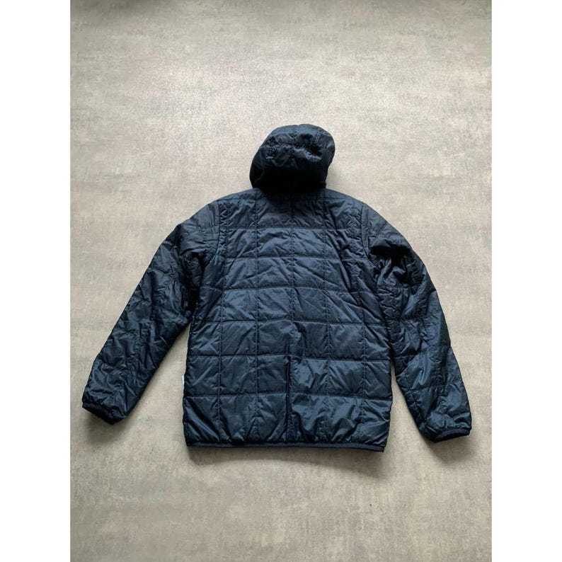 K&ouml;nnte beinhalten: Marineblaue Steppjacke mit Kapuze. Die Jacke hat ein rautenf&ouml;rmiges Steppmuster auf K&ouml;rper und &Auml;rmeln. Sie hat einen durchgehenden Rei&szlig;verschluss und lange &Auml;rmel. Die Jacke ist aus einem leichten Material gefertigt.