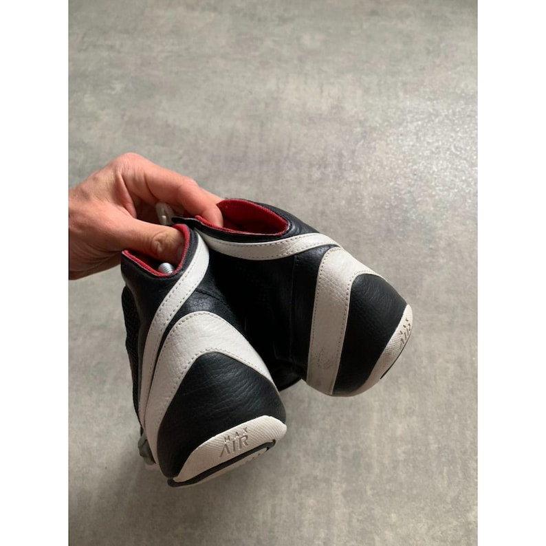 Puede incluir: Zapatillas deportivas negras y blancas con forro interior rojo. Las zapatillas presentan un dise&ntilde;o de rayas blancas curvas en los laterales y las palabras "MAX AIR" en la suela. Las zapatillas est&aacute;n sujetas por una mano.