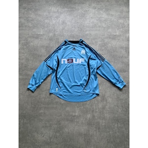 May include: Light blue long-sleeved soccer jersey with black accents. The jersey features the word "neuf" in white, a logo on the chest, and black stripes on the shoulders. The jersey is made of a lightweight material.