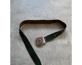 May include: A dark green leather belt with silver-colored studs and a decorative buckle. The buckle has a star design with orange and silver accents. The belt is brown on the inside.