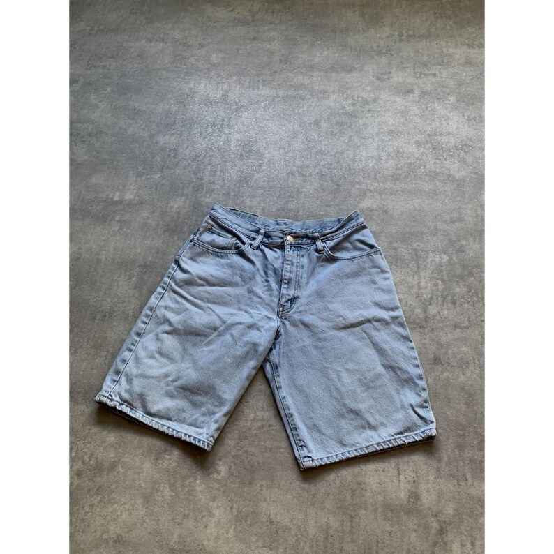 May include: Light blue denim shorts with a classic five-pocket design. The shorts have a button and zipper closure and a relaxed fit. The denim has a faded wash, giving them a vintage look. The shorts are suitable for casual wear.