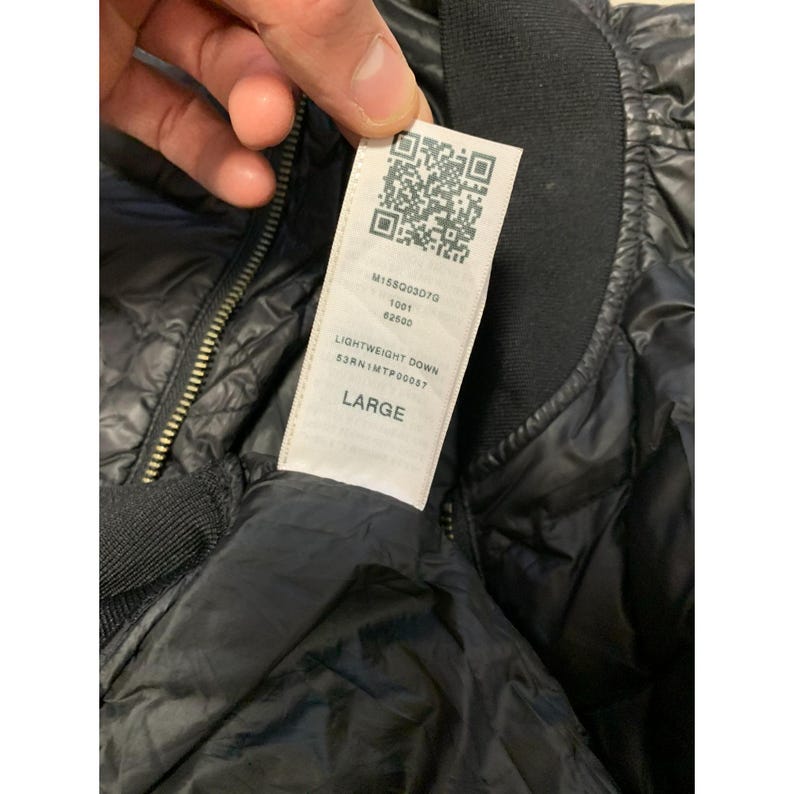 May include: Close-up of a black quilted bomber jacket with a black ribbed collar and a zipper. A white tag displays the text "LIGHTWEIGHT DOWN" and "LARGE". The jacket is made of a shiny, lightweight material.