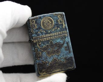 Isqueiro vintage em metal com pátina, estilo Zippo com gravuras orientais.