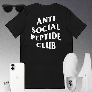 May include: Black t-shirt with the text "ANTI SOCIAL PEPTIDE CLUB" in white. The image also includes black sunglasses, a white smartphone, a small vial, and a pair of white slip-on sneakers.