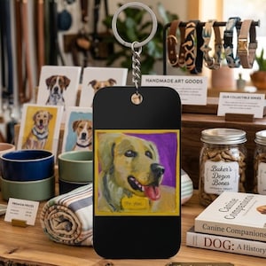 May include: A rectangular black keychain featuring a colorful painted portrait of a golden dog with its tongue out, set against a purple background. The dog wears a yellow collar tag with the text The Fool written in black ink on the surface.