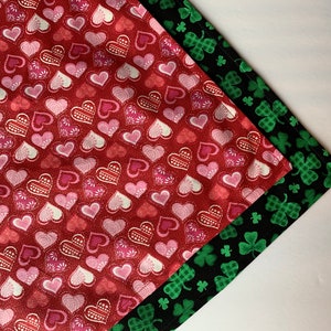 May include: Two folded fabric napkins. One is red with pink and white heart patterns. The other is black with green plaid shamrocks. The napkins are likely for seasonal or holiday use.