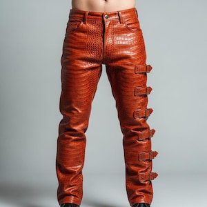 May include: Orange leather trousers with a crocodile skin texture. The trousers have a classic five-pocket design and feature multiple decorative buckles on the sides. The trousers are made of a shiny, textured material.