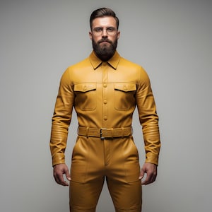 May include: A mustard yellow leather jumpsuit with a collared shirt-style top, two chest pockets, and a matching belt. The pants have pockets and the outfit is worn by a person with a beard and glasses.