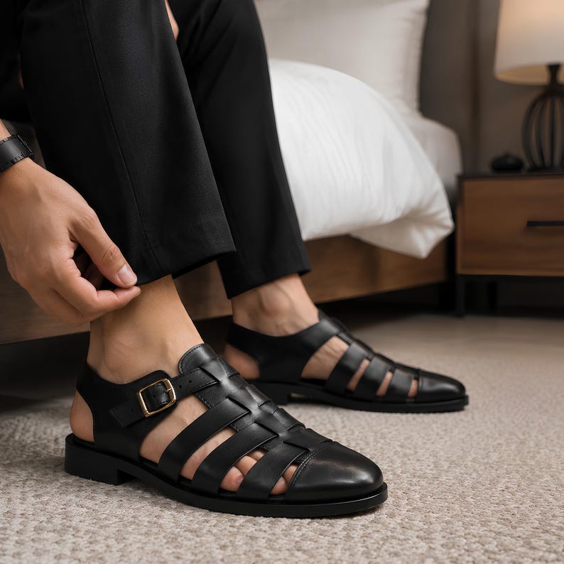 May include: Black leather fisherman sandals featuring a closed rounded toe, multiple wide straps across the upper, and an adjustable ankle strap with a gold-toned metal buckle. The footwear has a flat sole and an open heel design for ventilation.