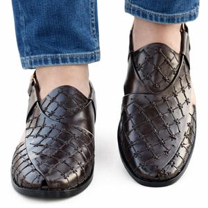 May include: A pair of dark brown leather sandals with a woven pattern. The sandals have a strap that goes around the ankle and are worn with blue jeans.