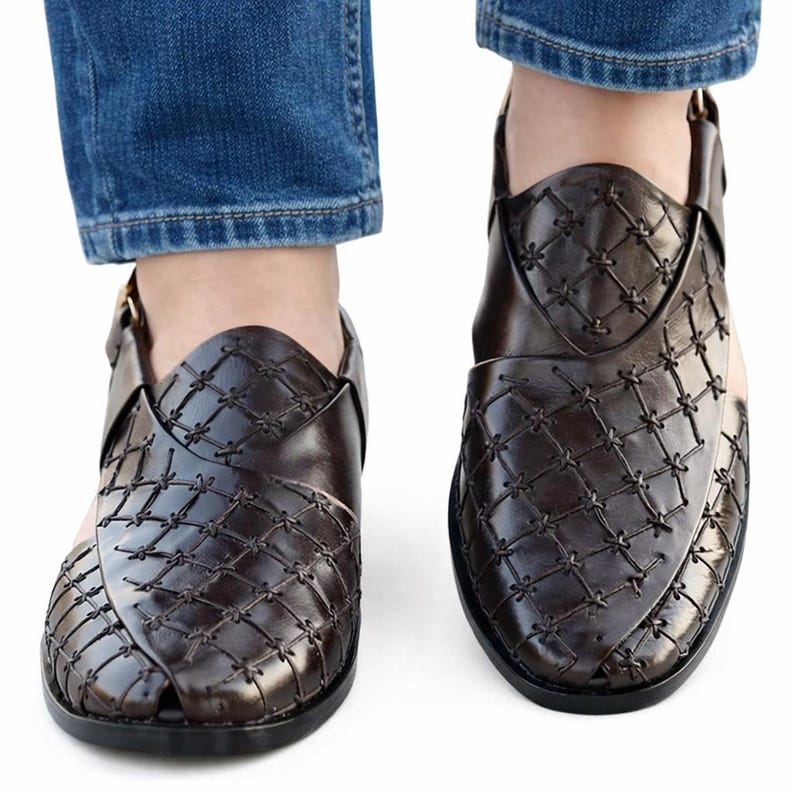 May include: A pair of dark brown leather sandals with a woven pattern. The sandals have a strap that goes around the ankle and are worn with blue jeans.