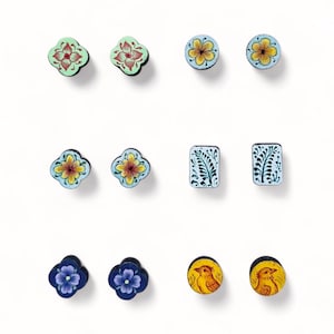 May include: A collection of hand-painted wooden earrings in various shapes and designs. The earrings feature floral and bird motifs in colors like red, yellow, blue, and green. The earrings are set against a white background.