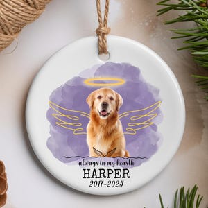 May include: A white ceramic ornament featuring a Golden Retriever with a halo and angel wings, set against a purple watercolor background. The text reads "always in my hearth HARPER 2017-2025". A jute twine loop is attached for hanging.
