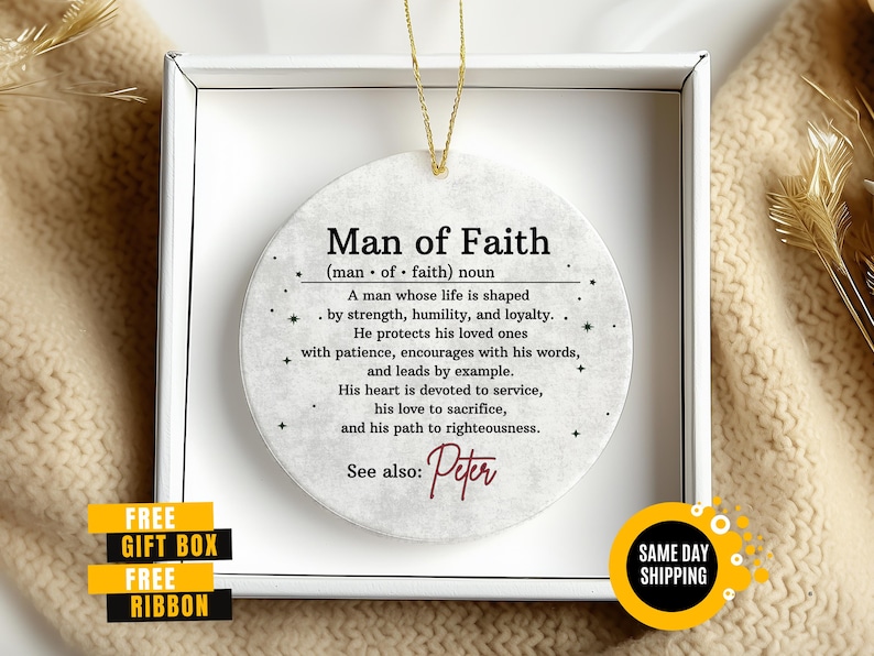 May include: A round, off-white ornament with the text "Man of Faith" and a definition. The ornament is in a white box with a gold string for hanging. Includes the name "Peter".