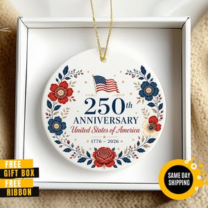 May include: A white ceramic ornament commemorating the 250th anniversary of the United States of America. The design features the American flag, floral elements in red and blue, and the text "250th Anniversary United States of America 1776-2026".